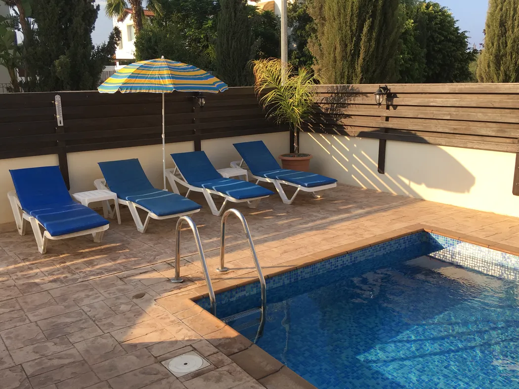 Palm Villa pool terrace in golden evening light — four sun loungers and parasol beside the private pool